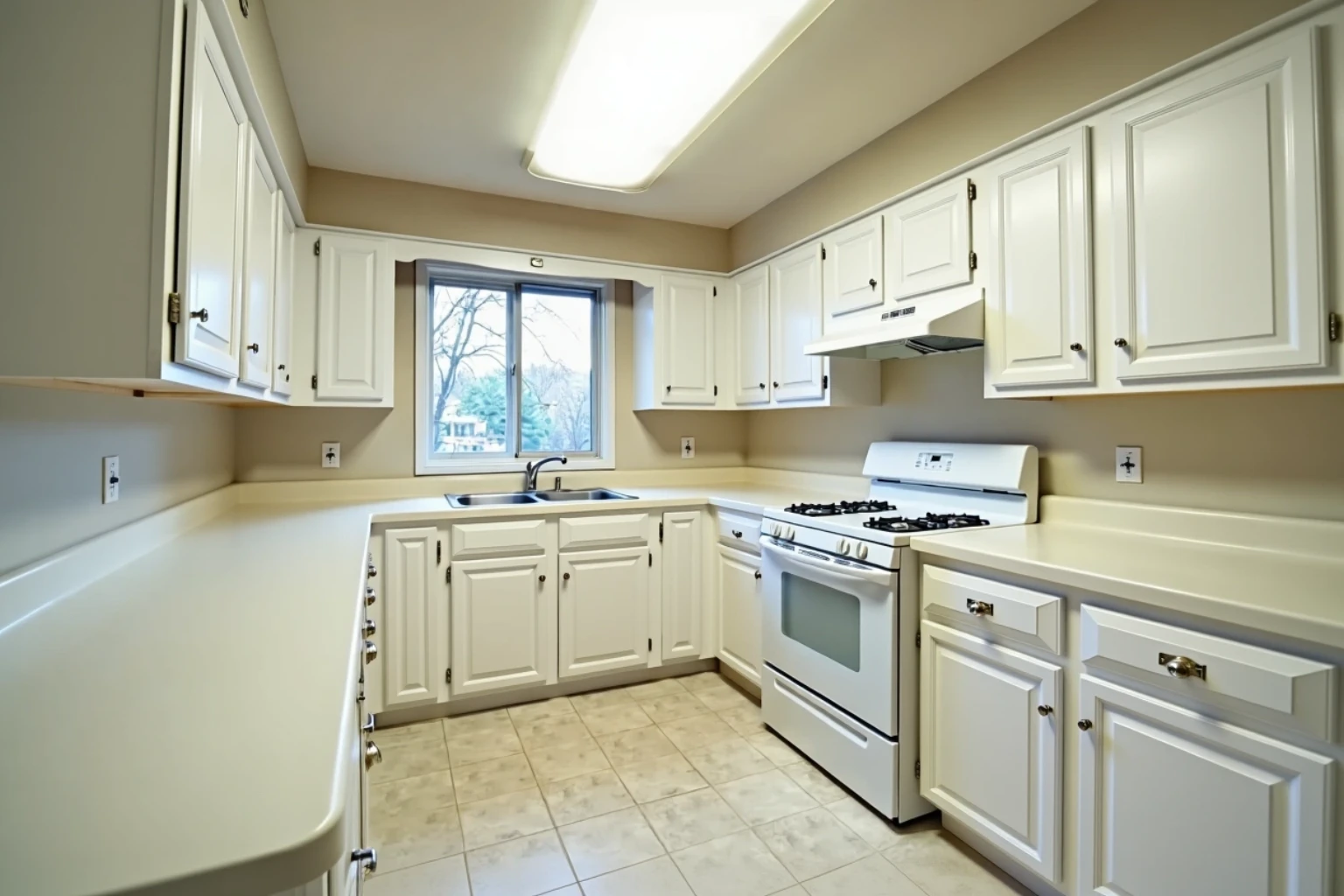 Same kitchen after refacing: white painted raised-panel doors and drawer fronts on the original boxes, counters and range unchanged.